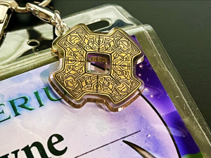 Picture of the Myst 5 tablet printed on an acrylic lanyard charm. It is attached above the upper right corner of a name tag.
